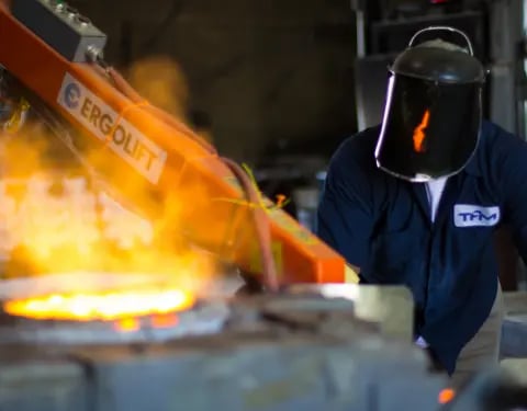 A factory worker in protective equipment works with heavy machinery